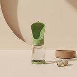 Nuzzo green 2-in-1 portable dog water bottle with integrated drinking bowl on a minimalist beige background.
